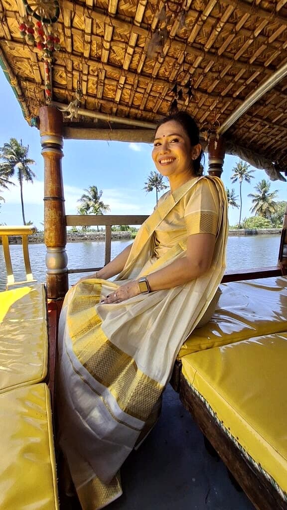 Woman wearing a traditional Kerala Kasavu saree seated inside an authentic bamboo-roofed shikara boat