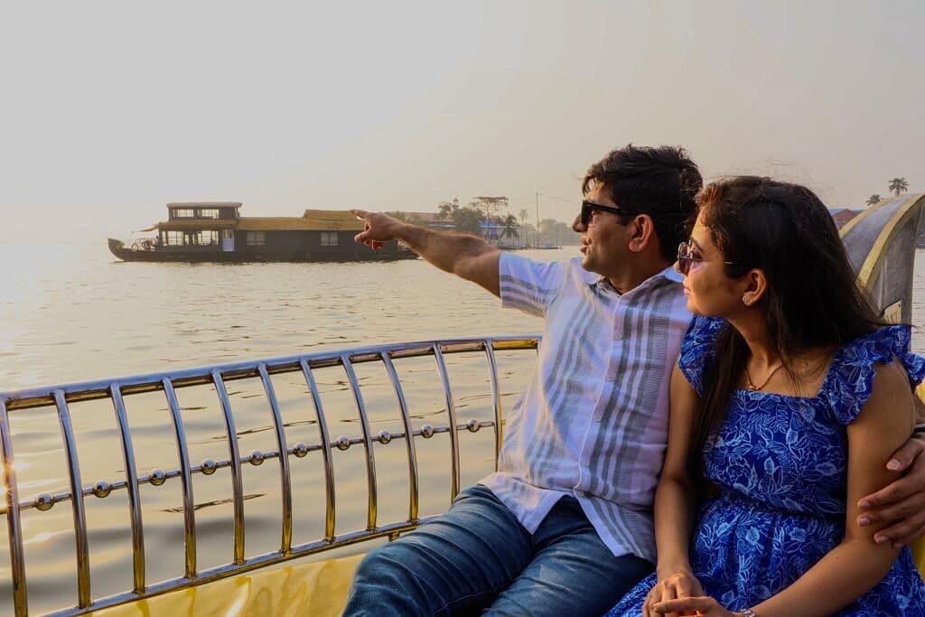Couple on a shikara boat watching a traditional kettuvallam houseboat glide past in golden afternoon light